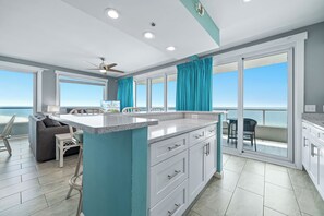 A modern kitchen with a large island, a dining area with a view, and a ceiling fan. - Silver Beach 801 | Beachfront & Dog-Friendly | Top Floor Corner Condo (Orange Beach)