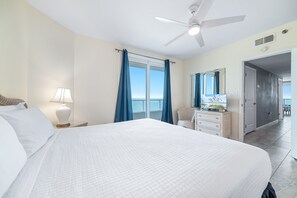 Ein Hotelzimmer mit einem Bett, einem Nachttisch, einer Lampe, einer Kommode, einem Spiegel und einem Deckenventilator.