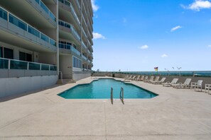 A swimming pool with lounge chairs, a building with multiple balconies, and a clear sky. - Silver Beach 801 | Beachfront & Dog-Friendly | Top Floor Corner Condo (Orange Beach)
