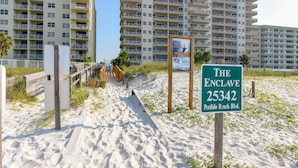 Ett hotell vid stranden som heter ”The Enclave”, med en skylt, en sandstig och ett trästaket.