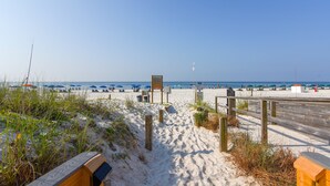 En sandstig som leder till havet, med strandparasoller och en träpromenad.