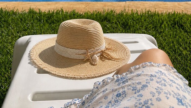 Zona piscina con una sedia a sdraio, un cappello di paglia e un ombrellone di paglia.