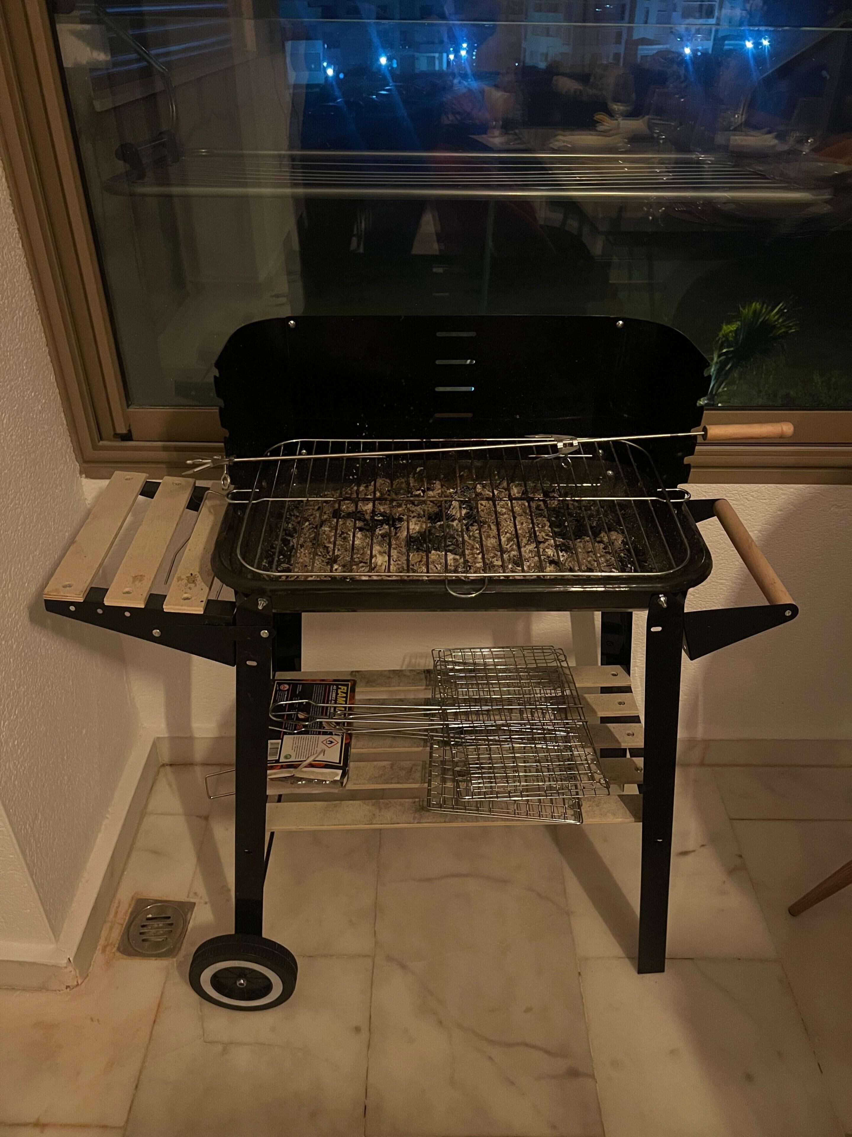 Una parrilla portátil con rejilla metálica, asa y estante de alambre debajo.