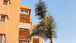 Un edificio residenziale a più piani con balconi, un prato curato e palme.