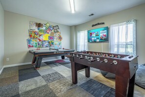 A room with two foosball tables, a TV displaying streaming services, and a wall decorated with educational materials. - LakePoint 4BR Retreat with Game Room (Cartersville)