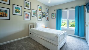 Ein Schlafzimmer mit einem Bett, Deckenventilator, einem Fenster mit Vorhängen und Stadtbildern in Rahmen an der Wand.