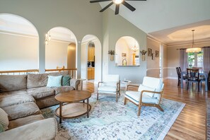 A spacious living room with a large sofa, a coffee table, and a dining area with chairs and a table. - LakePoint 4BR Retreat with Game Room (Cartersville)