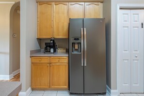 A kitchen with wooden cabinets, a stainless steel refrigerator, a coffee maker, and a water dispenser. - LakePoint 4BR Retreat with Game Room (Cartersville)