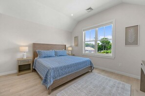 Un dormitorio con cama, ventana, mesita de noche y un cuadro colgado en la pared.