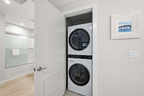A laundry room with two stacked washing machines, a glass shower enclosure, and a framed picture on the wall. - Bright Harwich Port Apartment close to beach (Harwich Port)