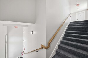 Eine Treppe mit hölzernem Geländer und Teppichstufen, die zu einer weißen Tür mit der Aufschrift 'EXIT' führt.
