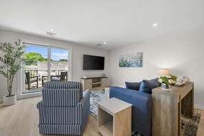 Ein modernes Wohnzimmer mit einem gestreiften Sessel, einem blauen Sofa, einem Holztisch und einem an der Wand montierten Fernseher.