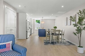 A modern kitchen with white cabinets and a dining area with a wooden table and chairs. - Charming Cape Apartment Walk to Beach & Town (Harwich Port)