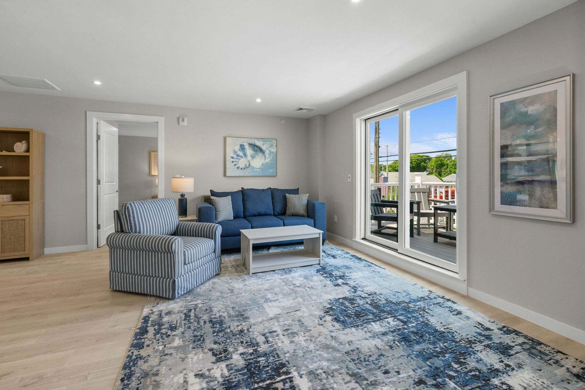 Un salon spacieux avec un canapé bleu, un fauteuil à rayures et une table basse. Une grande fenêtre offre une vue sur l’extérieur.