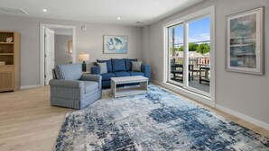 Een ruime woonkamer met een blauwe bank, een gestreept fauteuil en een salontafel. Een groot raam biedt uitzicht op het landschap.