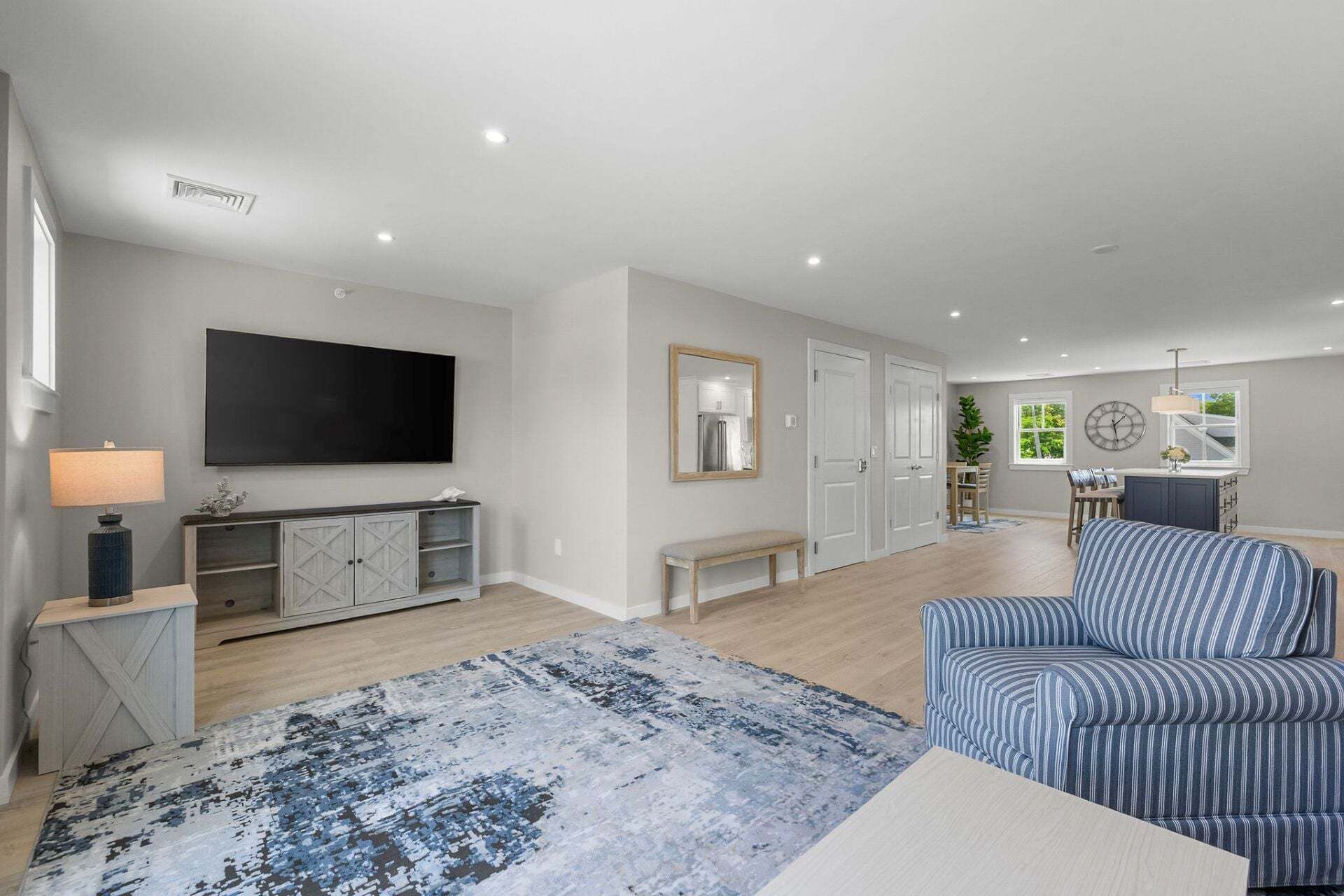 A spacious living area with a flat-screen TV, a bench, a patterned rug, and a striped sofa.