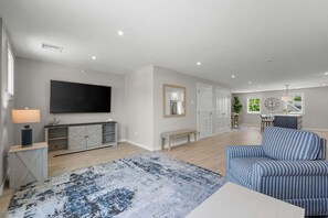 Ein geräumiger Wohnbereich mit Flachbildfernseher, einer Bank, einem gemusterten Teppich und einem gestreiften Sofa.