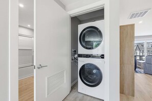 A laundry room with two front-loading washing machines, a door with a handle, and a view of the outside through a window. - Relaxing Harwich Port Apartment Near Beach & Downtown (Harwich Port)