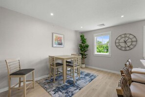 A dining area with a table and chairs, a potted plant, a clock, and a window with a view. - Relaxing Harwich Port Apartment Near Beach & Downtown (Harwich Port)