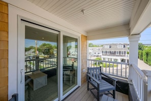 A balcony with a sliding glass door, a wooden deck, and a view of a residential street. - Beachside Harwich Port Apartment Near Town (Harwich Port)