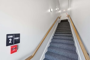A staircase leading to the first floor with a handrail on both sides and a fire pull handle on the wall. - Beachside Harwich Port Apartment Near Town (Harwich Port)