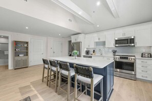 A modern kitchen with white cabinetry, a central island with bar stools, stainless steel appliances, and a wooden floor. - Beachside Harwich Port Apartment Near Town (Harwich Port)