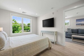 Ein Schlafzimmer mit einem Bett, einem Fernseher und einem Fenster mit Blick auf Grünfläche.
