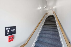 Eine Treppe führt zur ersten Etage, an beiden Seiten befindet sich ein Geländer und in der Wand ist ein Feuermelder angebracht.