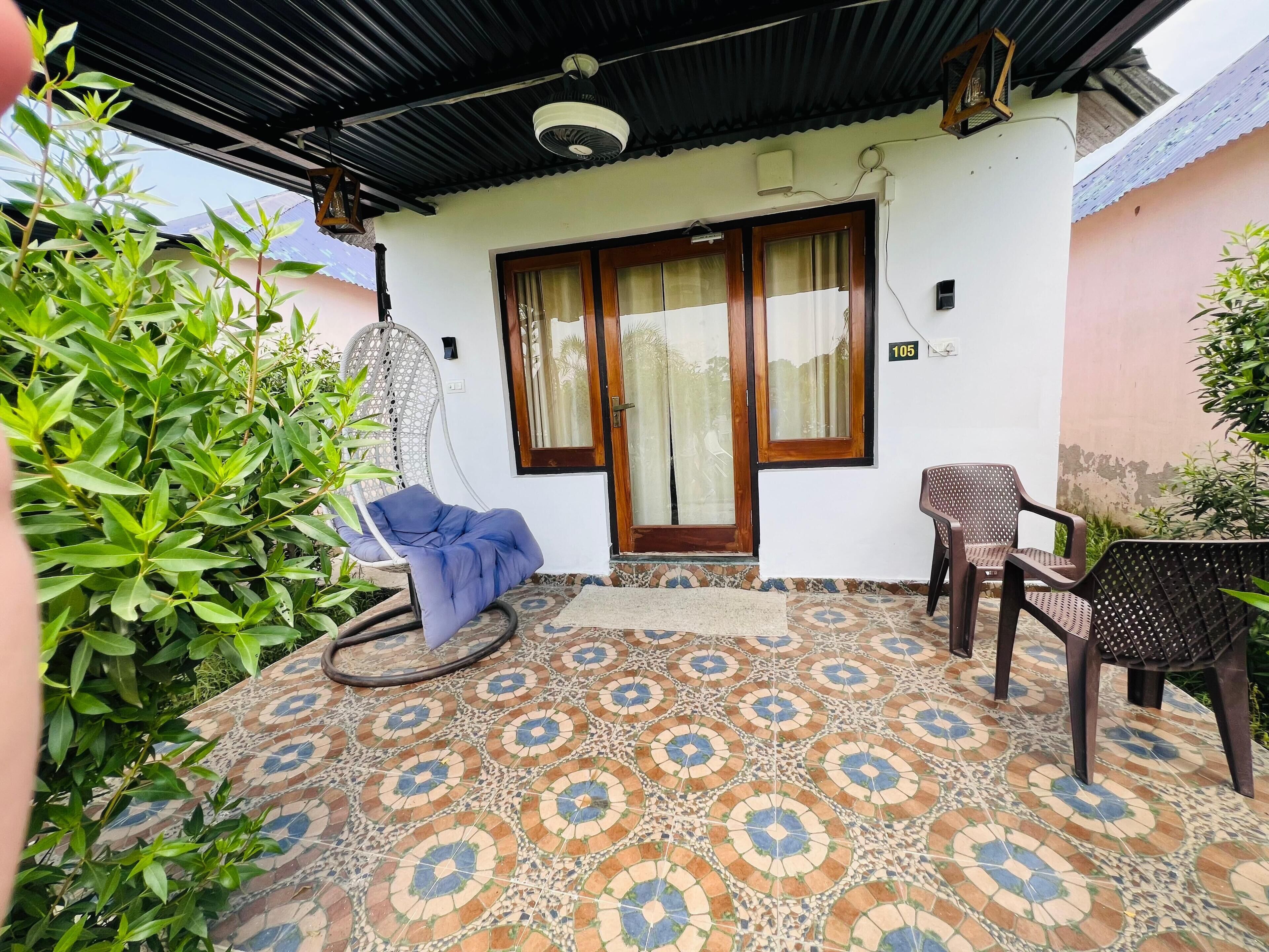Un patio techado con piso estampado, una silla azul, una mesa de madera y una hamaca colgante.