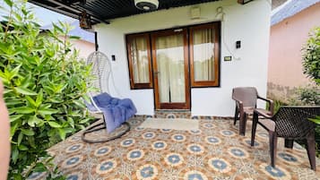 Un patio techado con piso estampado, una silla azul, una mesa de madera y una hamaca colgante.