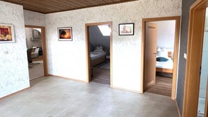Ein geräumiger Raum mit hoher Decke und Holzbalken, ein Bett mit Kissen, ein kleiner Tisch und ein Stuhl.
