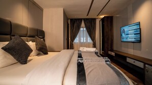 Habitación de hotel con una cama grande, televisor en la pared y vistas a la ciudad a través de la ventana.