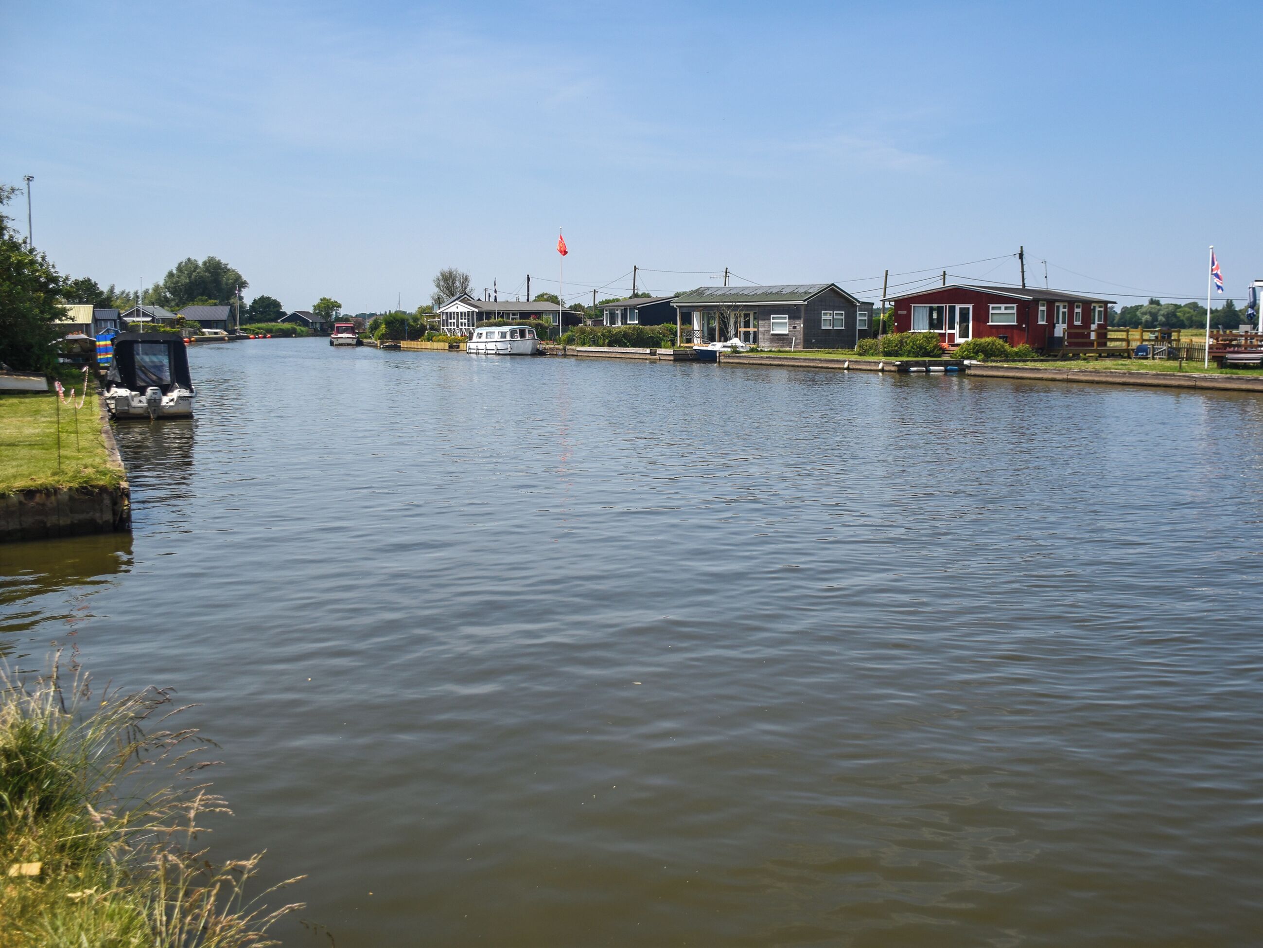 Une rivière paisible, avec des bateaux, des maisons et un drapeau sur la rive droite.