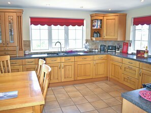 Een keuken met houten kastjes, een spoelbak en een eethoek met stoelen.