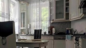 Een keuken met witte kasten, een eettafel met stoelen en een raam met gordijnen.