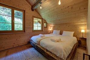 Ein Schlafzimmer in einer Holzhütte mit einem Bett, zwei Fenstern, einer Holzkονde und einem Nachttisch mit Lampe.