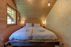 Ein Schlafzimmer einer Holzhütte mit zwei Betten, einem Fenster und einer Glühbirne.