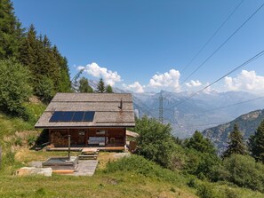 Eine Holzhütte mit Solaranlage, einer Terrasse und Blick auf die Berge.