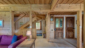 Um interior em madeira com escada, sofá, mesa e relógio.