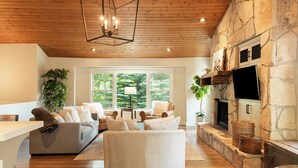 A living room with a stone fireplace, a large window, and a wooden ceiling. - 5BR Park City retreat with hot tub, fireplace, mountain views. (Park City)