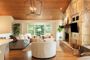 A living room with a stone fireplace, a large window, and a wooden ceiling. - 5BR Park City retreat with hot tub, fireplace, mountain views. (Park City)