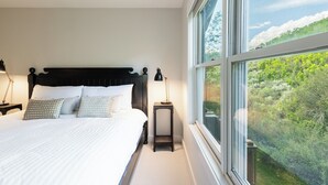 A bedroom with a large bed, a nightstand, a lamp, and a window with a view of greenery. - 5BR Park City retreat with hot tub, fireplace, mountain views. (Park City)