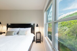 A bedroom with a large bed, a nightstand, a lamp, and a window with a view of greenery. - 5BR Park City retreat with hot tub, fireplace, mountain views. (Park City)