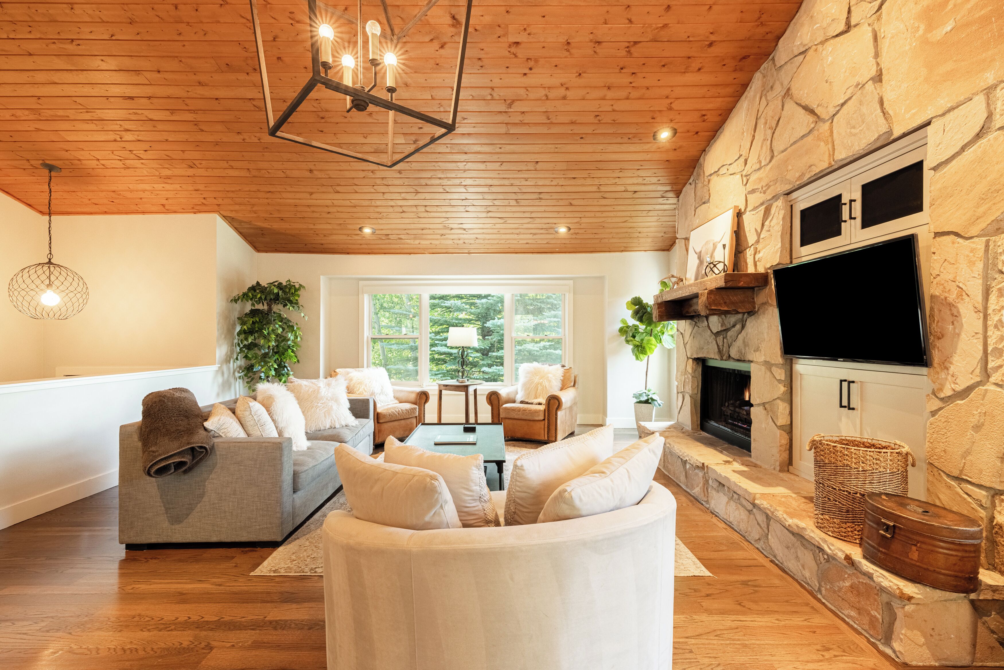 Una sala de estar acogedora con chimenea de piedra, techo de madera y un televisor de pantalla plana grande.