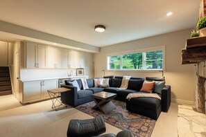 Ein modernes Wohnzimmer mit einem Ecksofa, einem Couchtisch und Blick auf einen Garten durch ein Fenster.