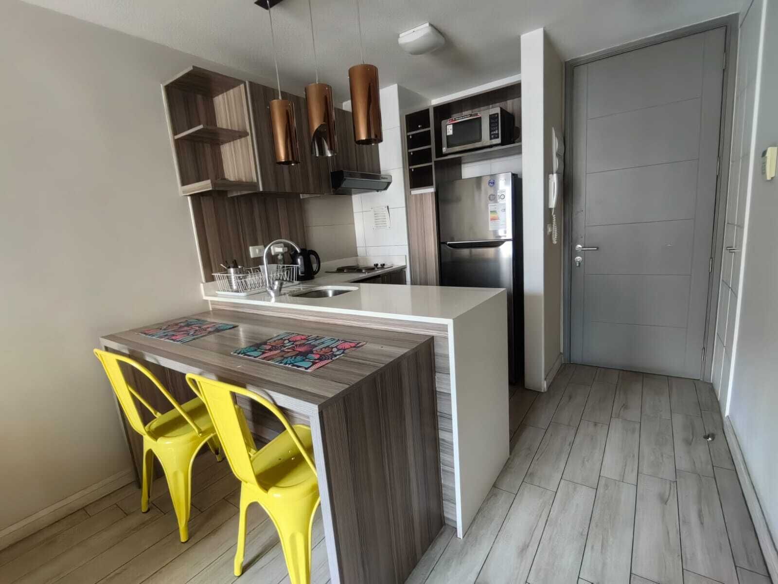 Una cocina compacta con una isla central, microondas, refrigerador y pileta.