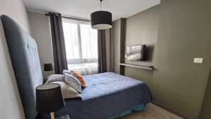A bedroom with a bed, a bedside lamp, a TV on the wall, and a window with curtains. - Santa Lucía, Downtown Central Santiago (Santiago)
