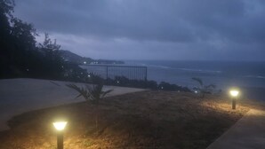 Escena costera nocturna con un paseo empedrado, una baranda metálica y dos faroles iluminados.