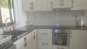 Cocina con gabinetes blancos, horno de acero inoxidable, lavavajillas y ventana con vista a follaje.