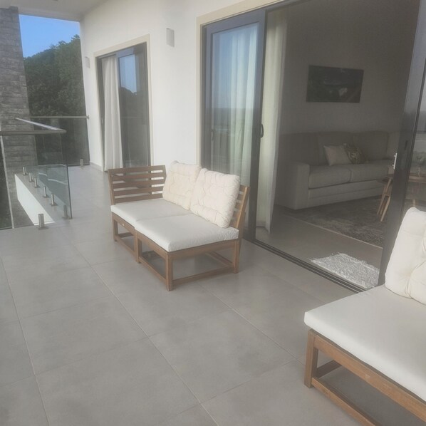 Ein modernes Wohnzimmer mit einer Couch und einem Sessel, eine Glastür, die zu einem Balkon führt, und eine Treppe.